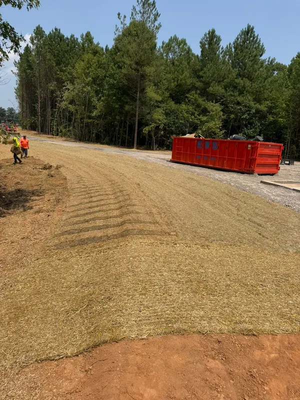 Graded slope seeded and covered in straw, crew working the far end