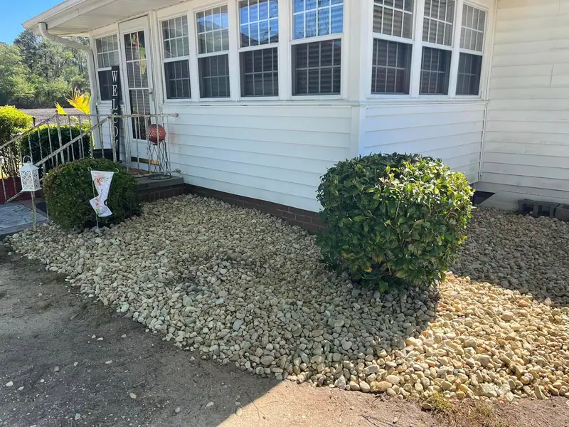River rock bed and a shaped shrub by a porch